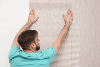 Photo of Man hanging stylish wall paper sheet indoors