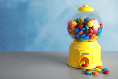 Candy machine with colorful treats on grey table. Space for text