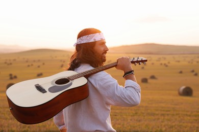 Photo of Portrait of happy hippie man with guitar in field, space for text