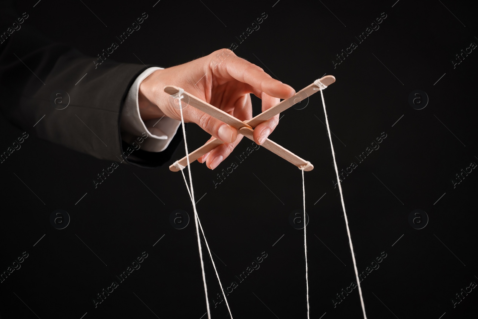 Photo of Woman pulling strings of puppet on black background, closeup