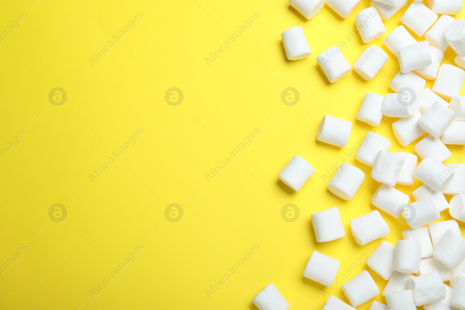 Photo of Delicious puffy marshmallows on yellow background, flat lay. Space for text