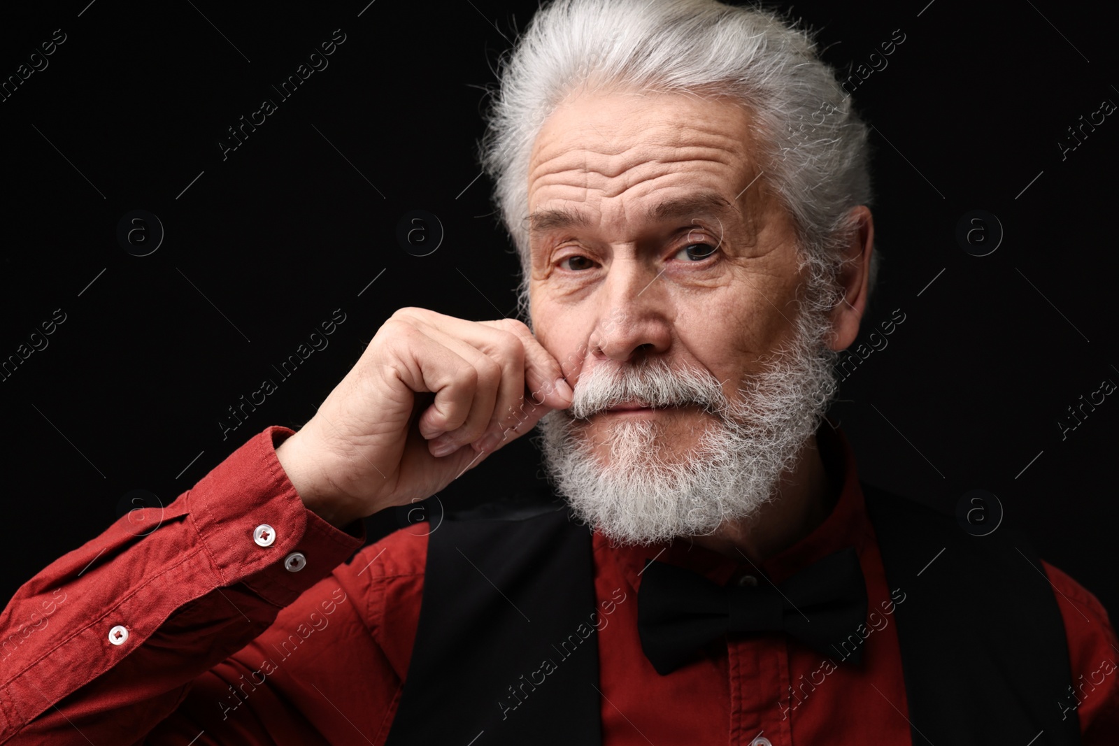 Photo of Senior man touching mustache on black background