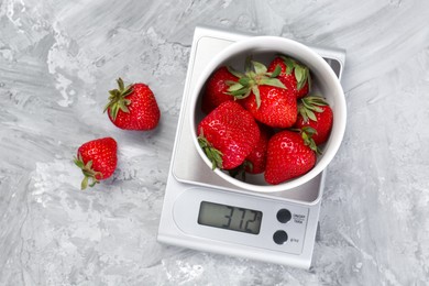 Kitchen scale with bowl of strawberries on grey textured table, flat lay