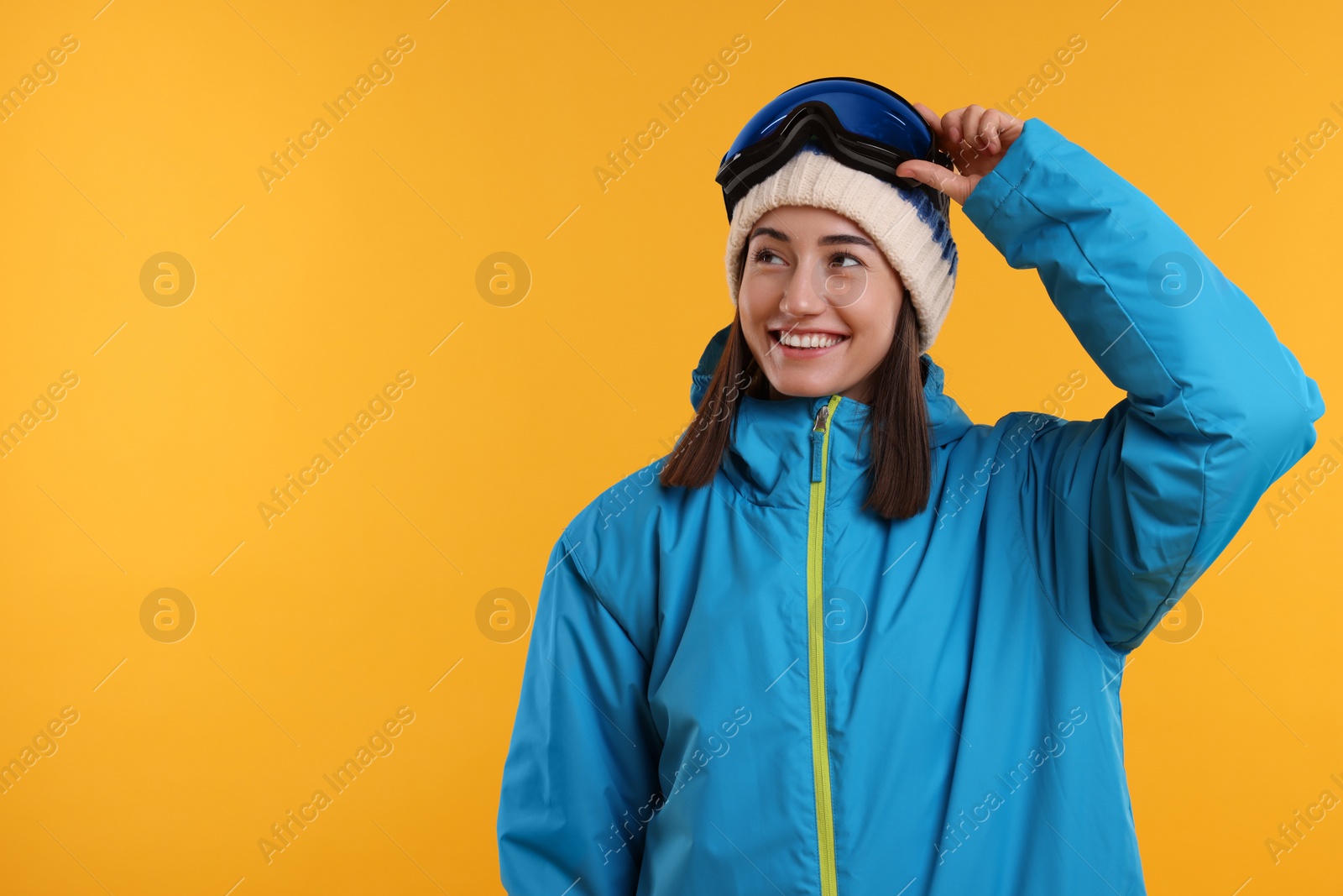 Photo of Winter sports. Happy woman with snowboard goggles on orange background, space for text