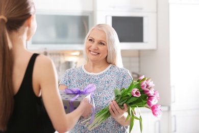 Daughter congratulating happy mature woman on Mother's Day at home