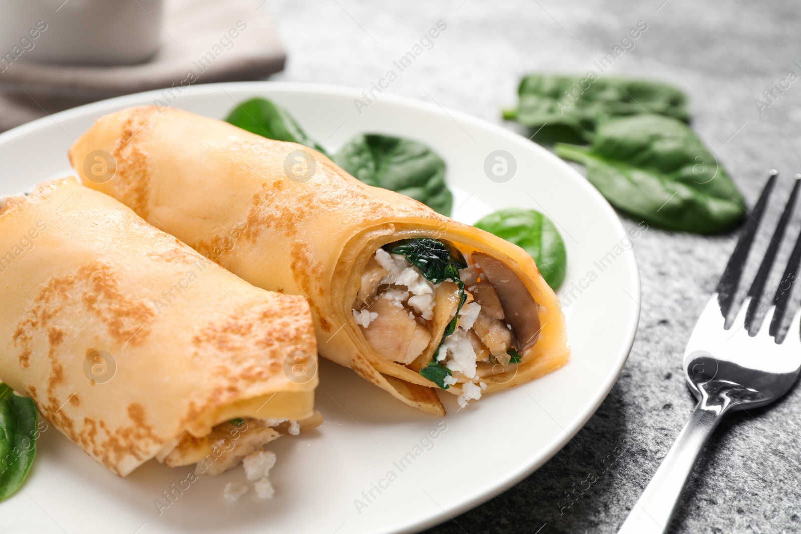 Photo of Delicious thin pancakes with chicken and mushrooms on grey table, closeup