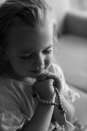 Cute little girl with beads praying indoors. Black and white effect