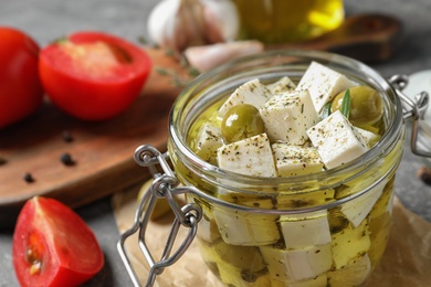 Composition with pickled feta cheese in jar on grey table, closeup