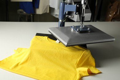 Photo of Printing logo. Heat press with yellow t-shirt on white table, space for text
