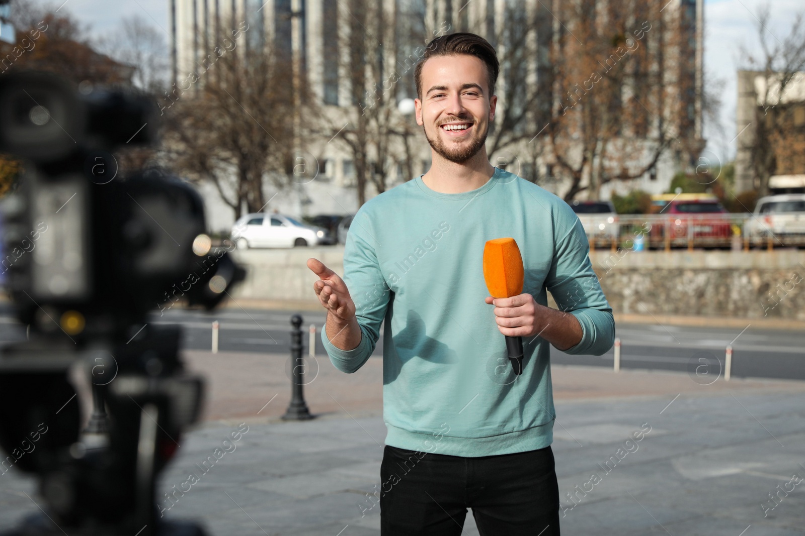 Photo of Young male journalist with microphone working on city street