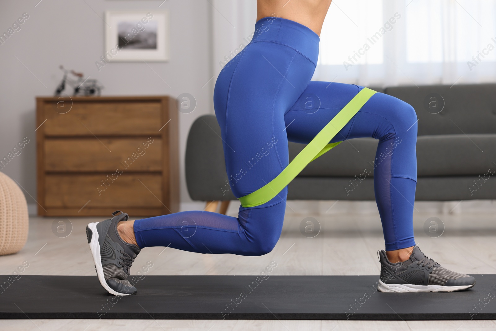 Photo of Woman doing exercise with fitness elastic band on mat at home, closeup