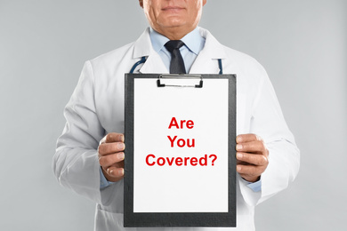 Image of Doctor holding clipboard with text ARE YOU COVERED? on light background, closeup. Insurance concept