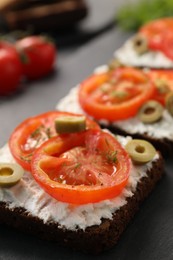Photo of Delicious ricotta bruschettas with sliced tomatoes, olives and greens on black table, closeup