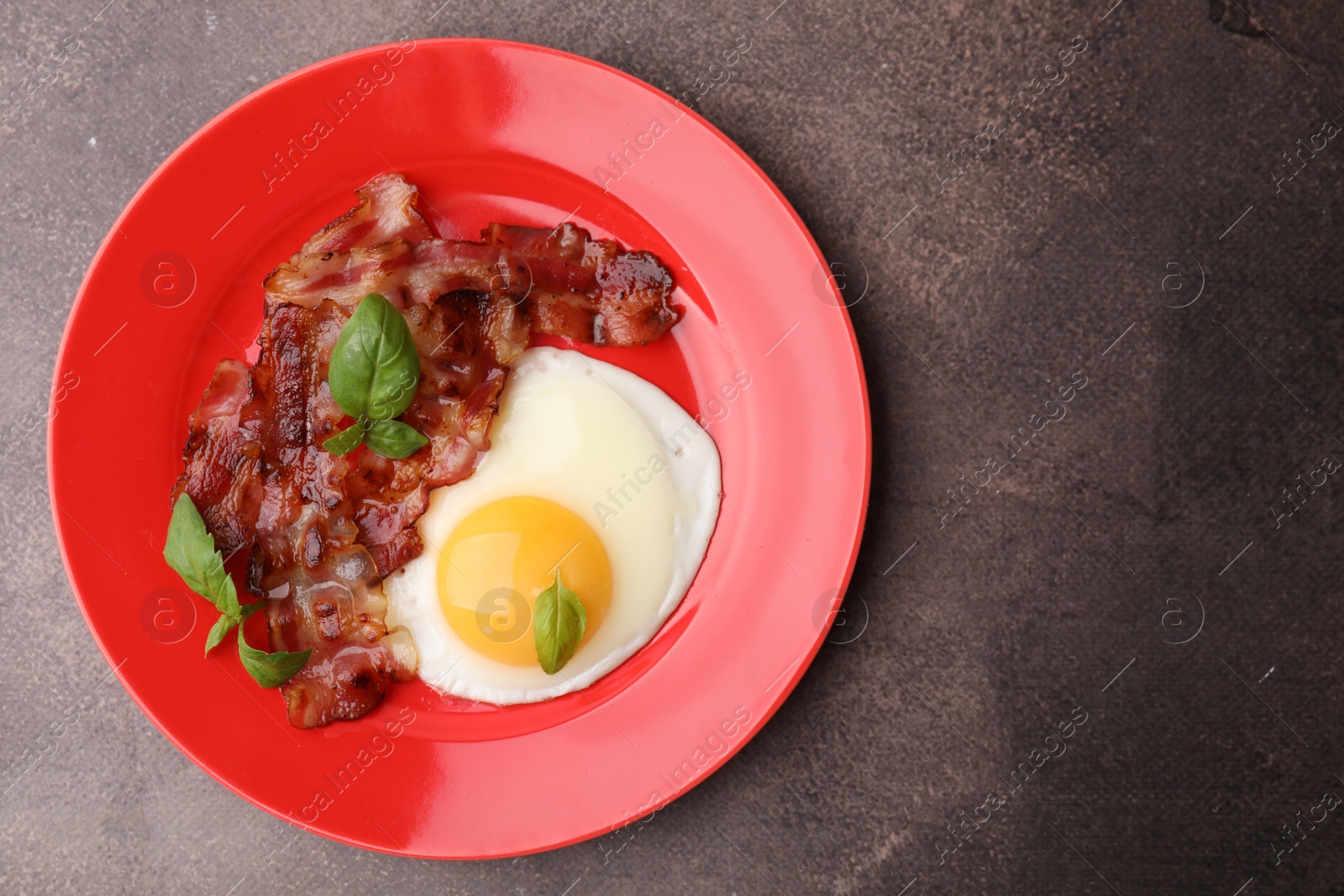 Photo of Fried egg, bacon and basil on brown table, top view. Space for text