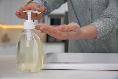 Photo of Woman washing hands with liquid soap in kitchen, closeup