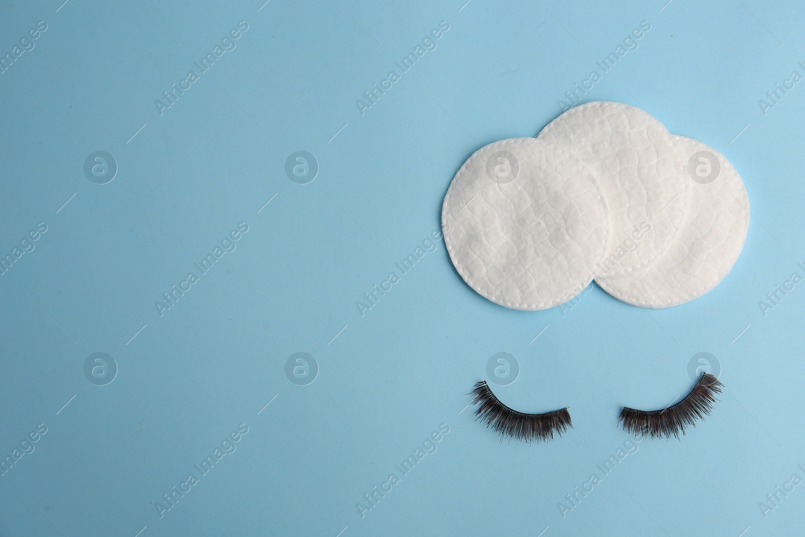 Photo of Cotton pads for makeup removal and false eyelashes on light blue background, flat lay. Space for text