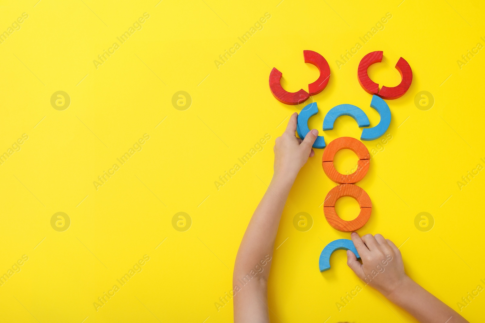 Photo of Motor skills development. Boy playing with colorful wooden arcs at yellow table, top view. Space for text