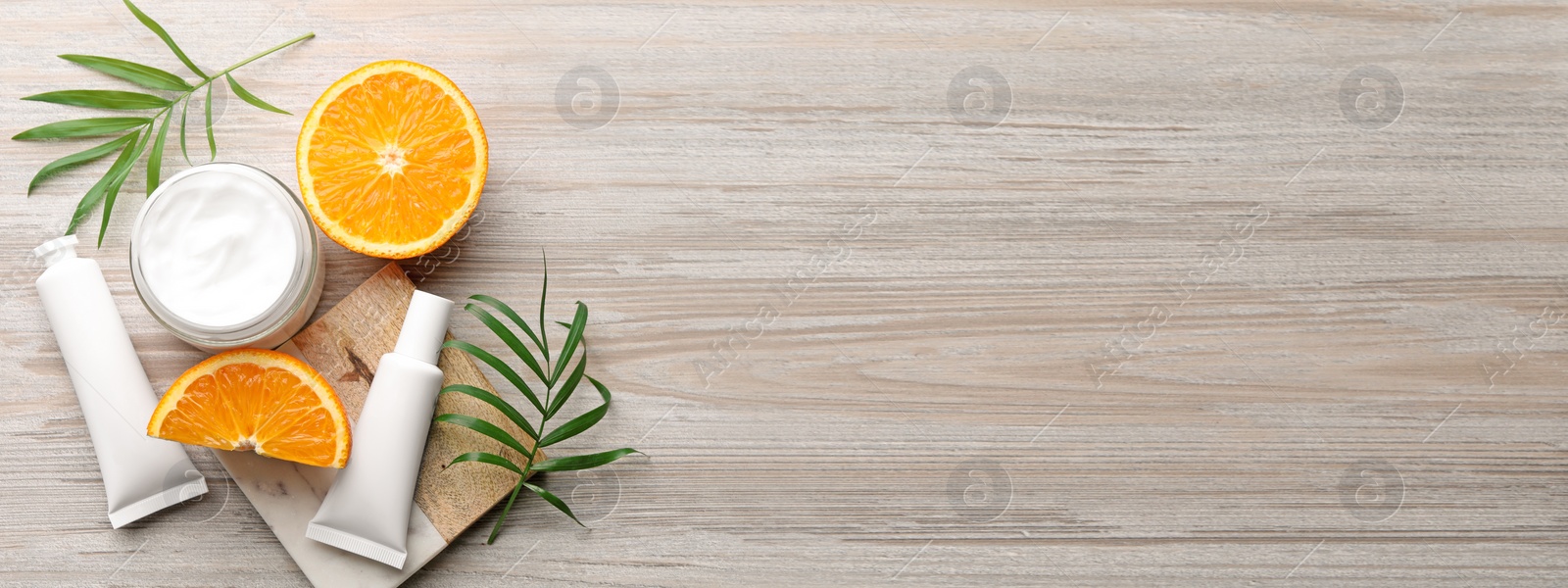 Image of Different hand care cosmetic products, orange and green leaves on white wooden table, flat lay with space for text. Banner design