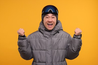 Photo of Winter sports. Excited man with ski goggles on orange background