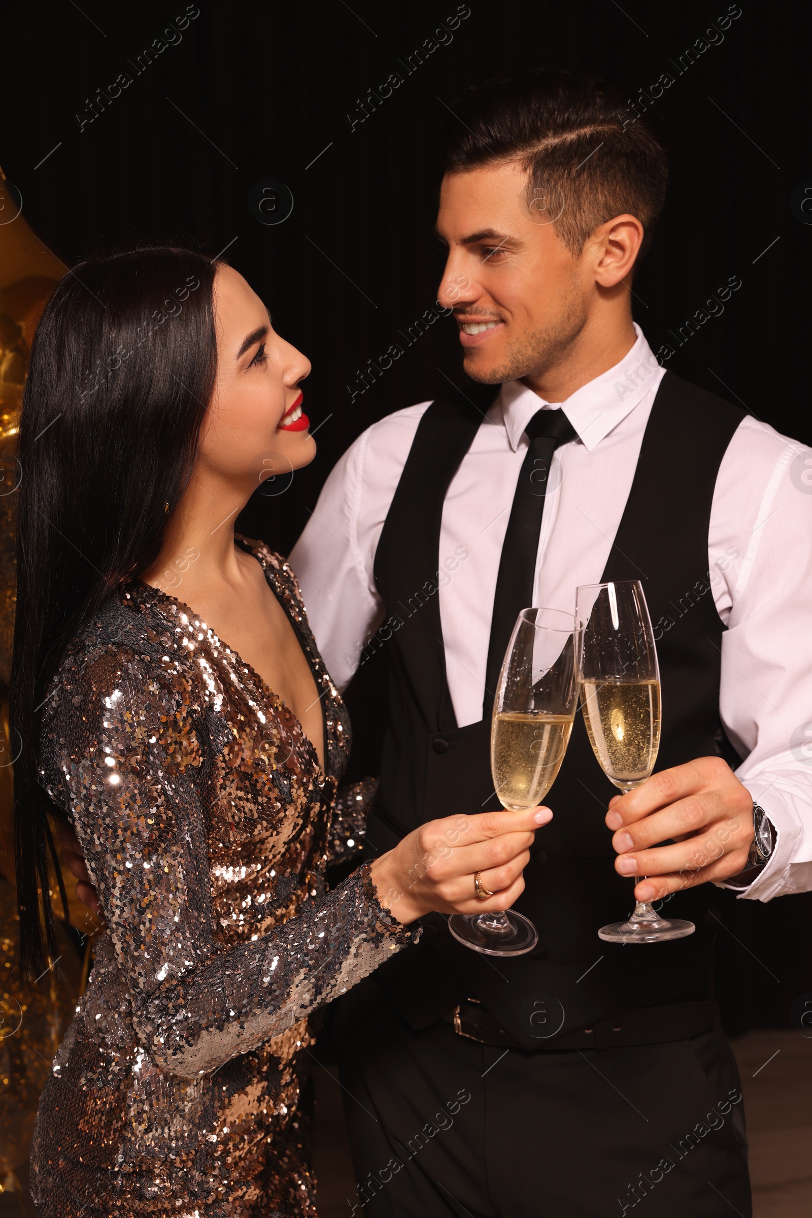 Photo of Happy couple with glasses of sparkling wine celebrating New Year on black background