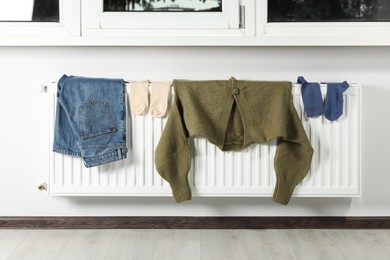 Photo of Jeans, socks and cardigan on heating radiator near window indoors