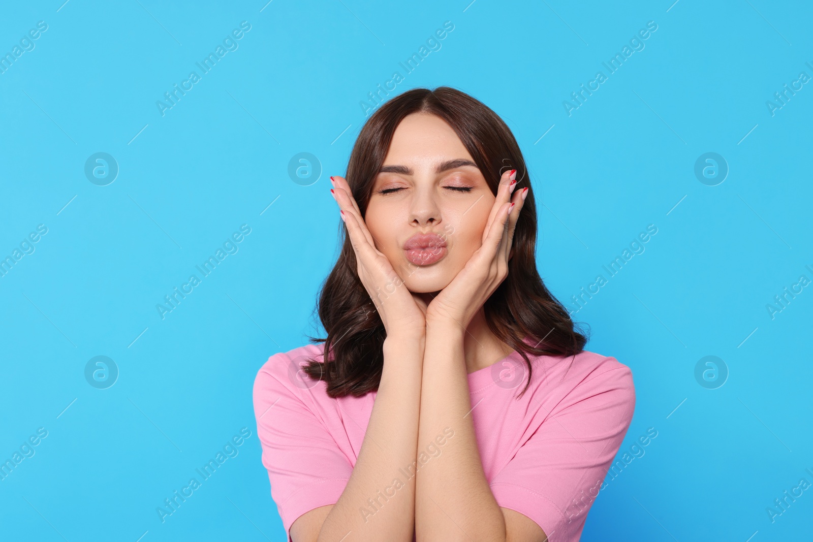 Photo of Beautiful young woman giving kiss on light blue background