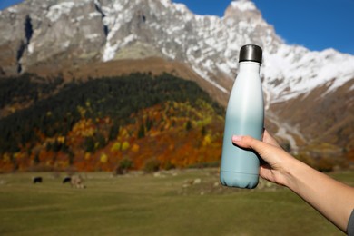 Woman holding thermo bottle with drink in mountains on sunny day. Space for text