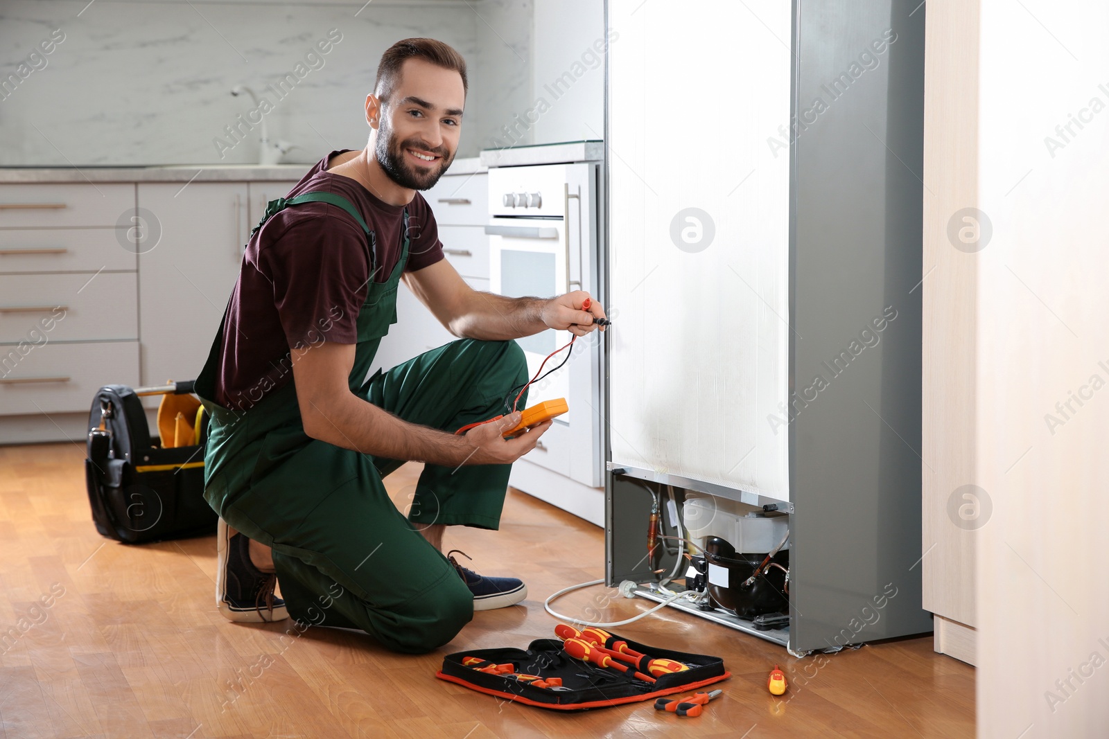 Photo of Male technician in uniform repairing refrigerator indoors