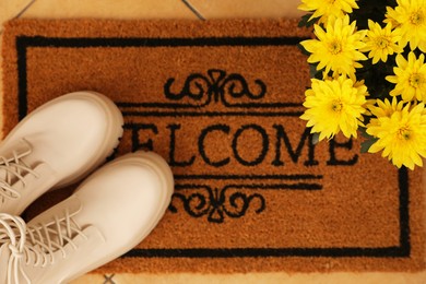 Photo of Door mat with word Welcome, stylish boots and beautiful flowers on floor, flat lay