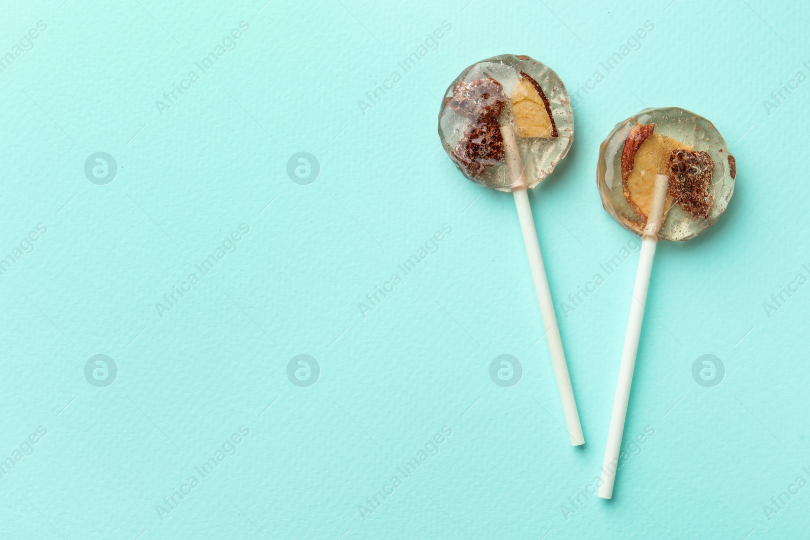 Photo of Sweet colorful lollipops with berries on turquoise background, flat lay. Space for text