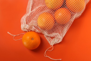 Photo of Net bag with fresh oranges on color background, top view