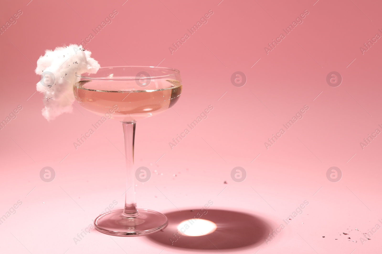 Photo of Tasty cocktail in glass decorated with cotton candy on pink background, space for text