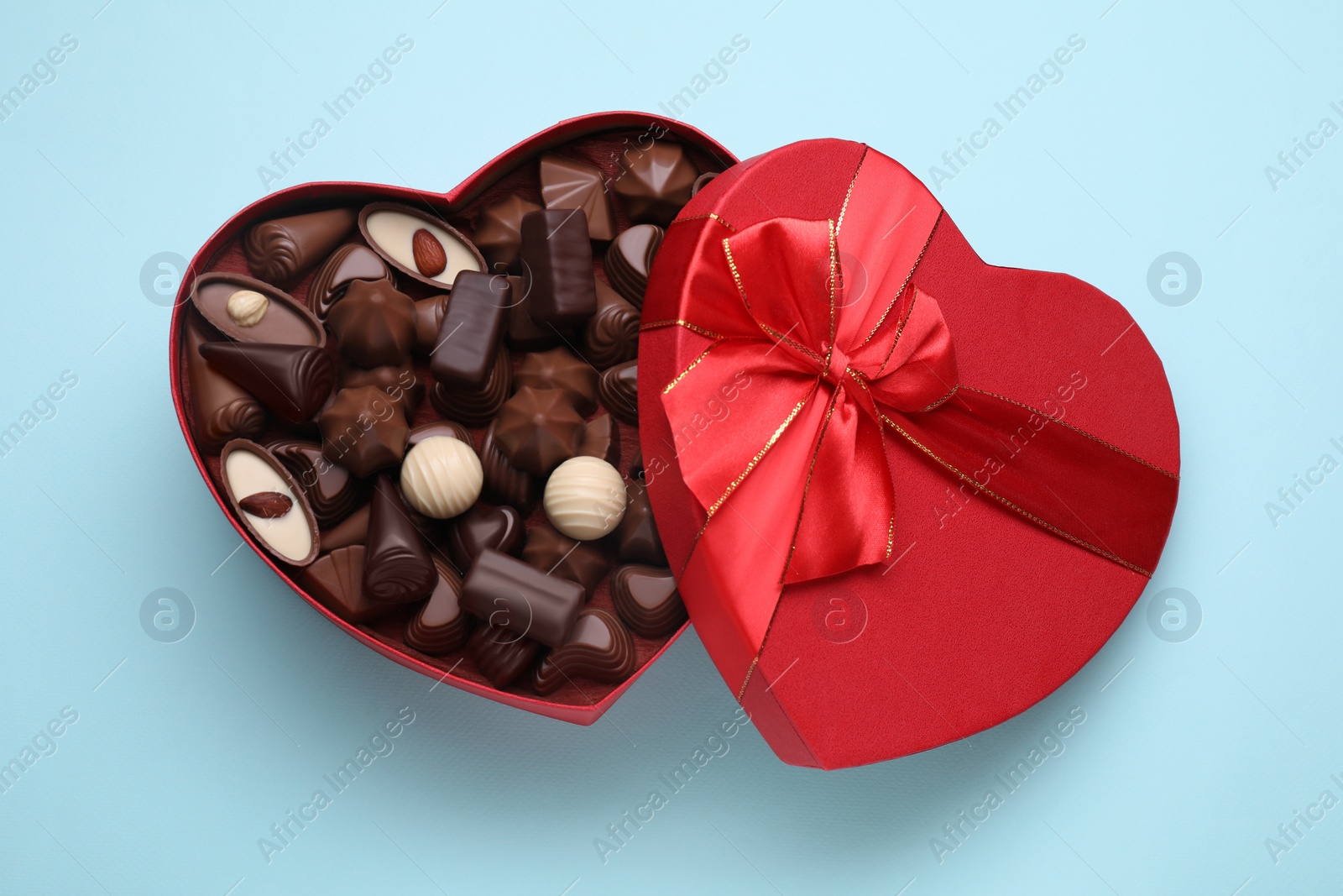 Photo of Heart shaped box with delicious chocolate candies on light blue background, top view