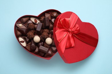 Heart shaped box with delicious chocolate candies on light blue background, top view