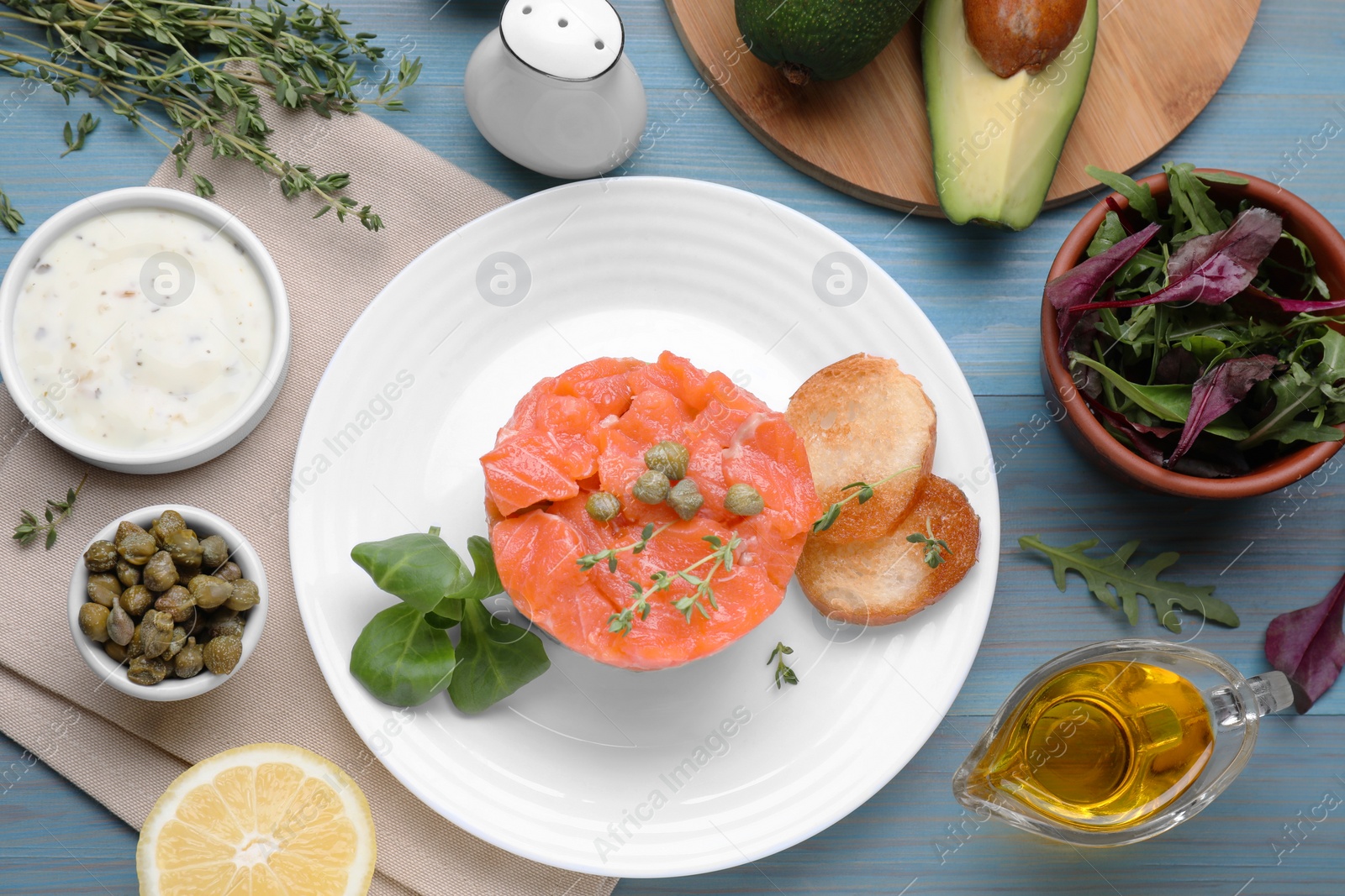 Photo of Delicious salmon tartare with croutons on light blue wooden table, flat lay