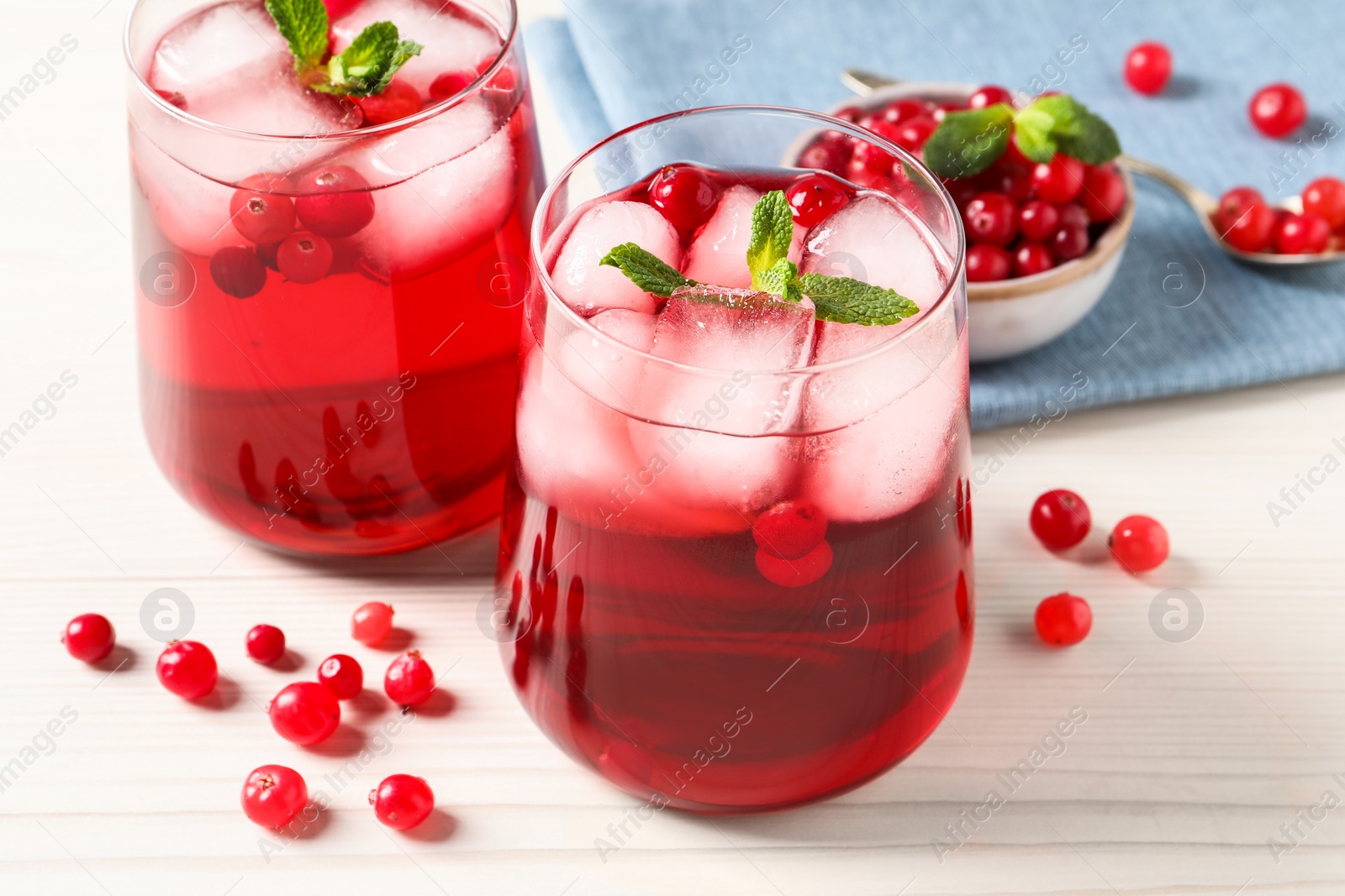 Photo of Tasty cranberry juice with ice cubes in glasses and fresh berries on white wooden table, closeup