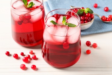 Photo of Tasty cranberry juice with ice cubes in glasses and fresh berries on white wooden table, closeup