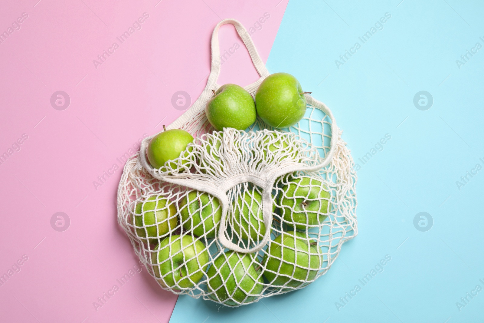 Photo of Mesh bag with ripe apples on color background, flat lay