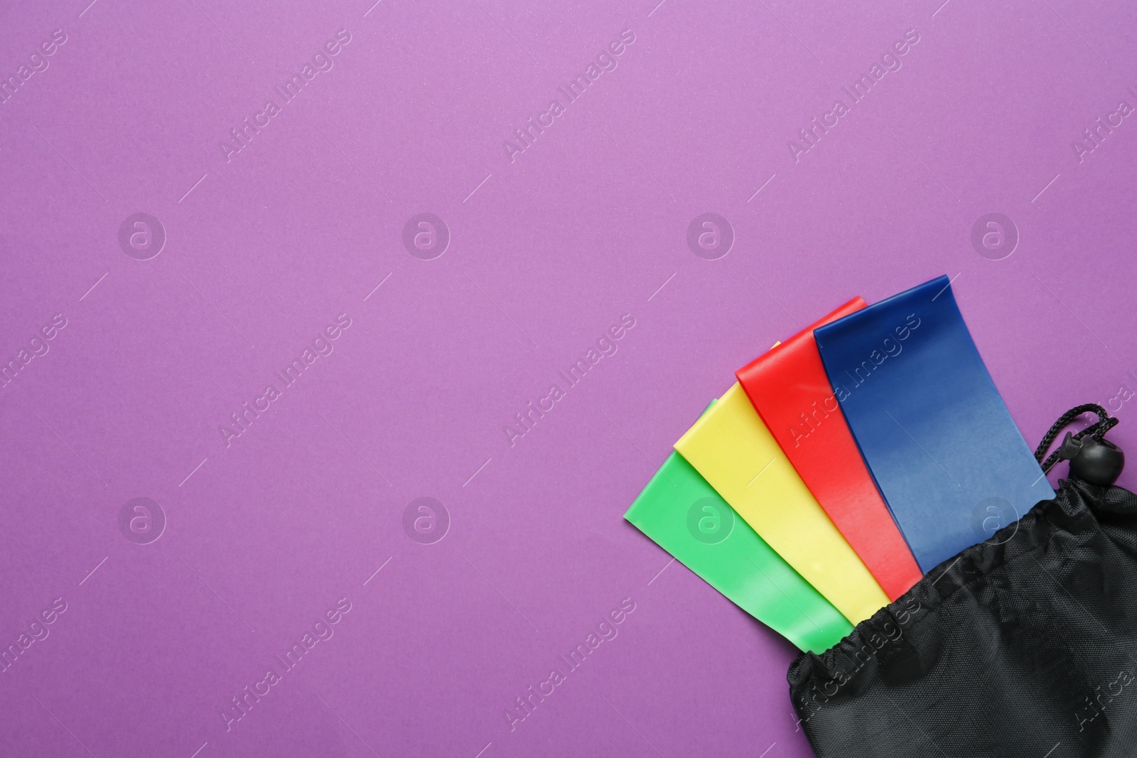 Photo of Set of fitness elastic bands in bag on purple background, top view. Space for text