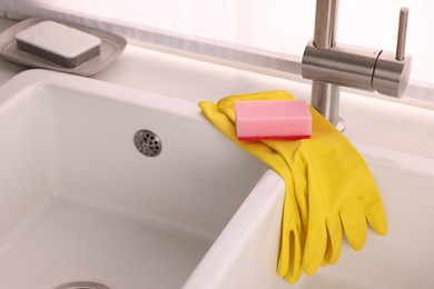 Photo of Sponge and rubber gloves on kitchen sink indoors