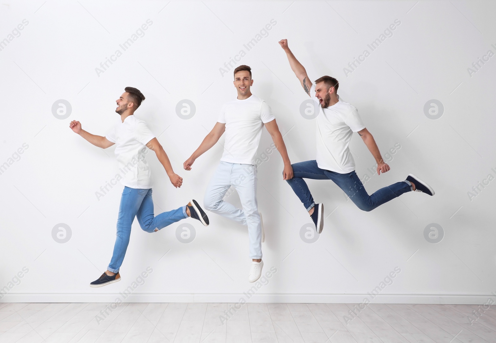 Photo of Group of young men in jeans jumping near light wall