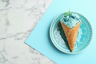 Plate with delicious spirulina ice cream cone on marble table, top view. Space for text