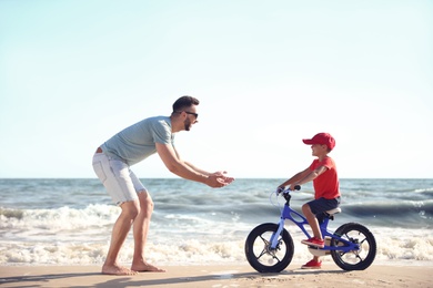 Happy father teaching son to ride bicycle on sandy beach near sea