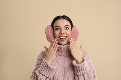 Beautiful young woman wearing earmuffs on beige background