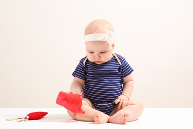 Photo of Little girl with sippy cup and toy carrot on light background. Baby accessories