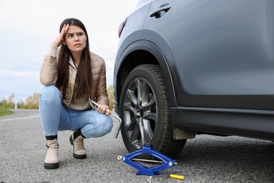 Worried young woman near car with punctured wheel on roadside