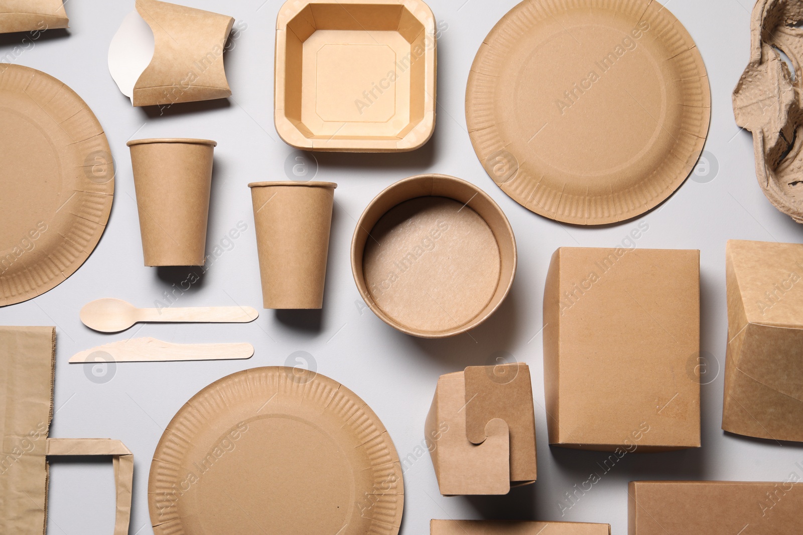 Photo of Eco friendly food packaging. Paper containers, bag and tableware on light grey background, flat lay