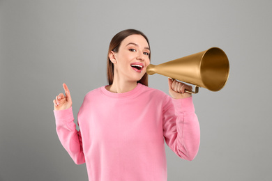 Young woman with megaphone on grey background