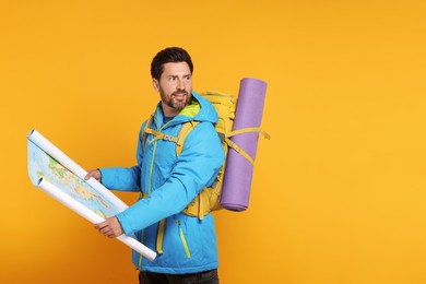 Photo of Happy man with backpack and map on orange background, space for text. Active tourism