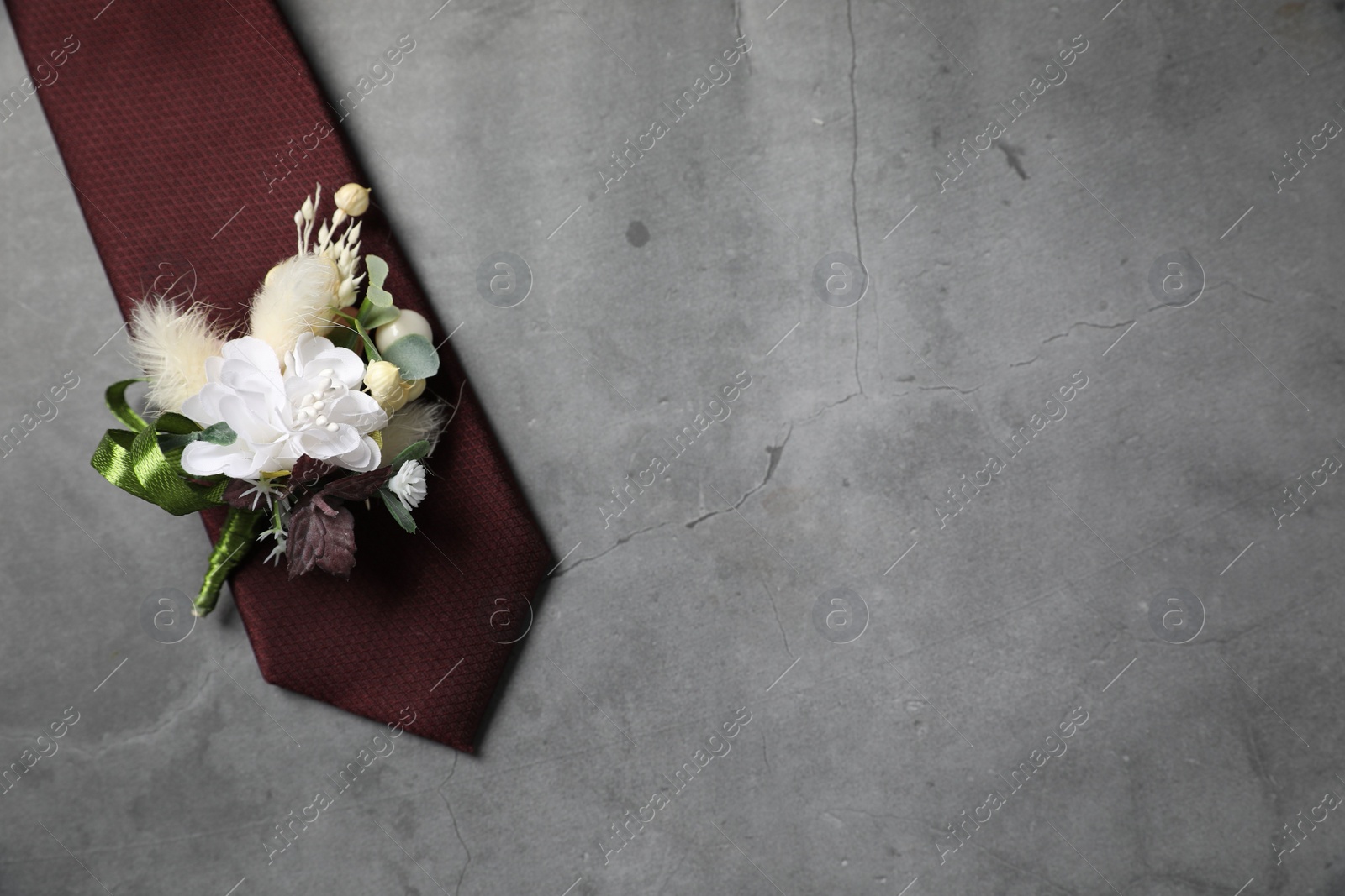 Photo of Wedding stuff. Stylish boutonniere and tie on gray background, top view. Space for text
